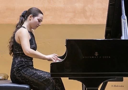 Angela Todorova playing a Steinway grand piano in a black gown