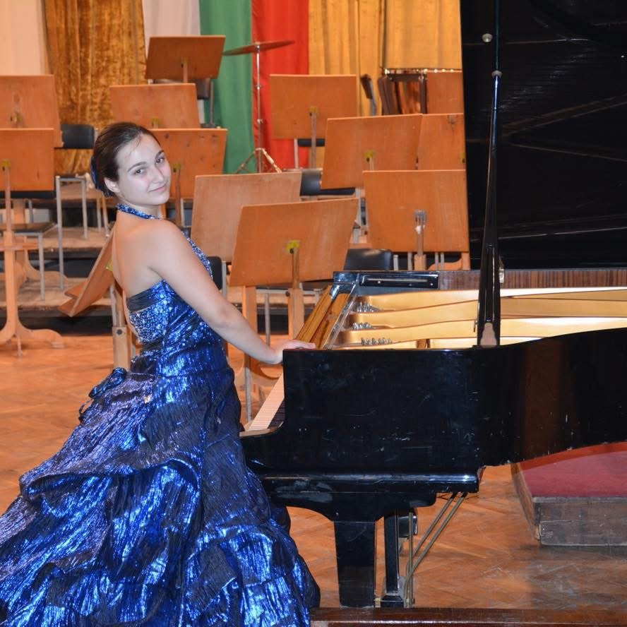 Angela Todorova in a blue gown beside a grand piano on stage