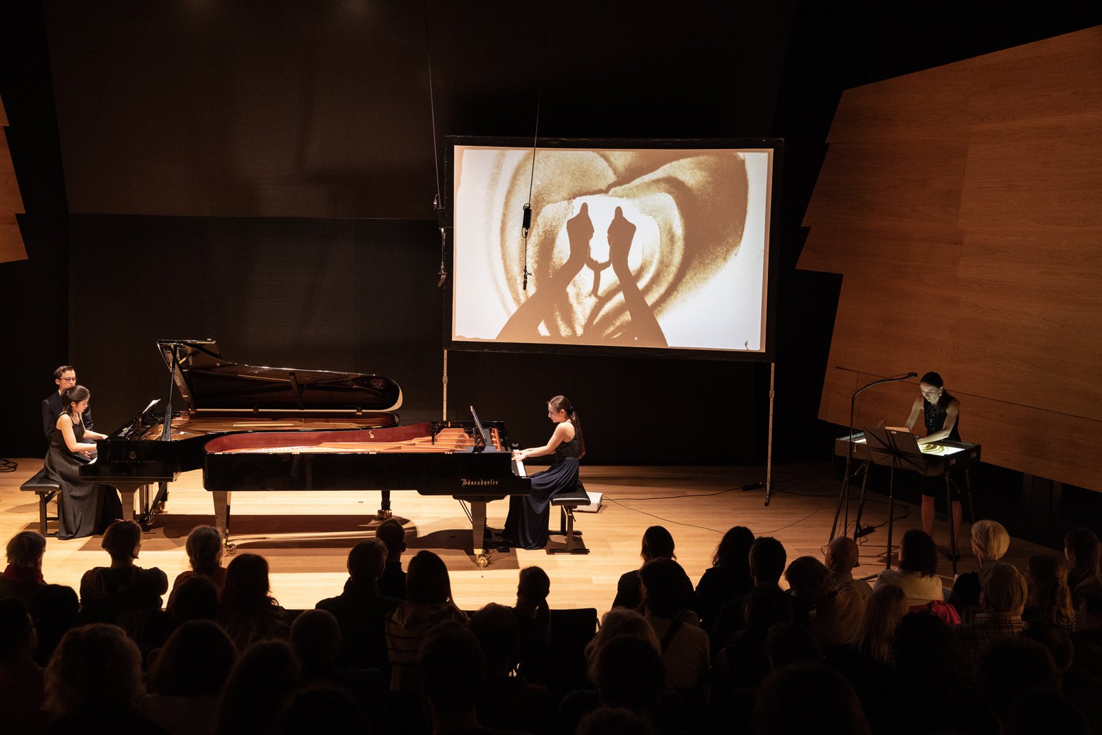 Two grand pianos on stage beneath a sand-animation screen at the MDW in Vienna