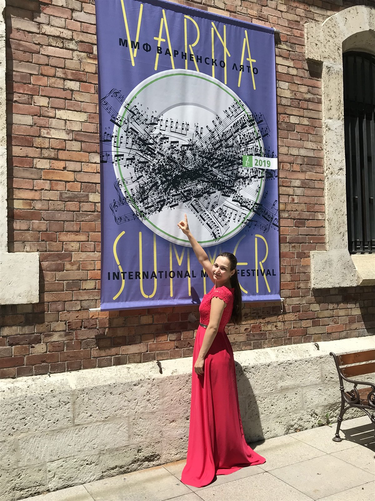 Angela Todorova in a red gown pointing at the Varna Summer festival banner